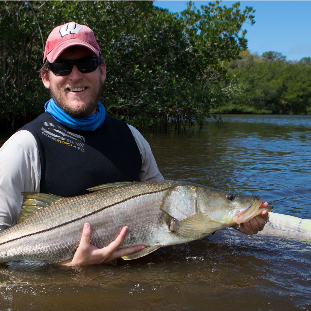 A Mote scientist smiles and holds a common snook, a popular fisheries species, in southwest Florida waters