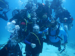 An underwater group photo featuring a dozen divers posing close together for the camera. Mote President and CEO, Dr. Michael Crosby is in the middle.