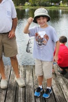 A young boy in a fishing hat proudly holds a line from which dangles a small catfish. A Mote volunteer stands close behind.