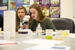 Two Riverview high school students peer through a microscope to study the life cycle of rotifers. 