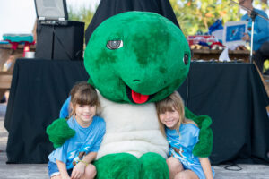 Tied 1 mile walk/run female winners, Brooke and Chloe Cicilioni, both age 7, sit with Mote Mascot Shelley the Sea Turtle after the race. 