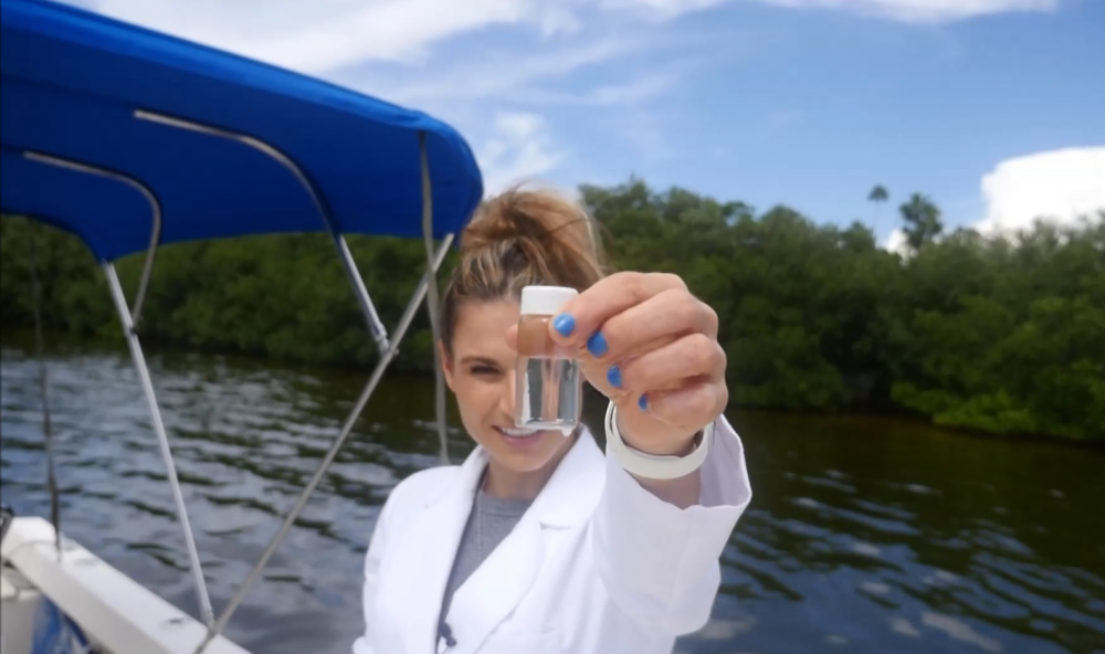 Mote scientist Tracy Fanara holds up a water sample that will be tested for Red Tide algae. She is out on a boat surrounded by mangroves.