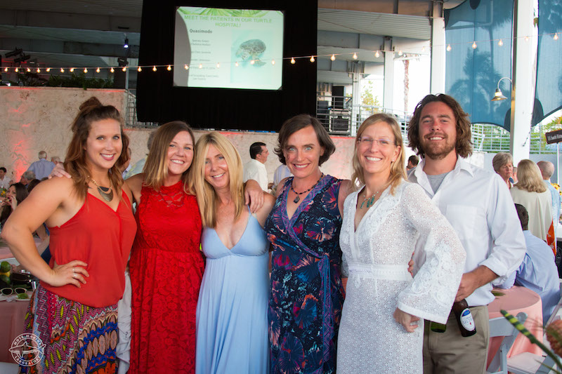 Six party goers pose for the camera with a slide highlighting Mote's Turtle Hospital projected in the background. They are Mote Hospital staff enjoying the evening with big smiles, fine clothes and great food.