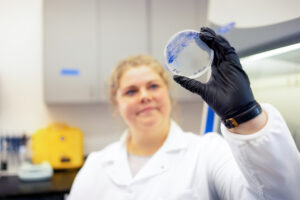 Dr. Kirstie Francis holds up a petri dish with blue microbial cultures growing on it.