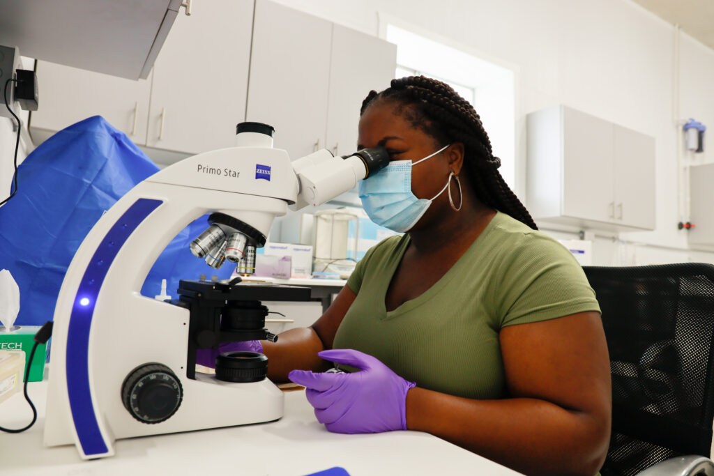 A young black woman examines a sample through a microscope.