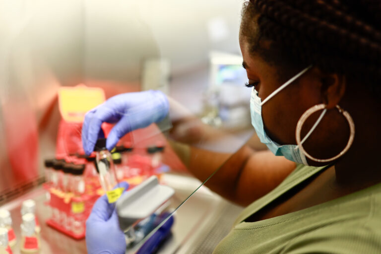 A black woman handles test tube samples in a laboratory.