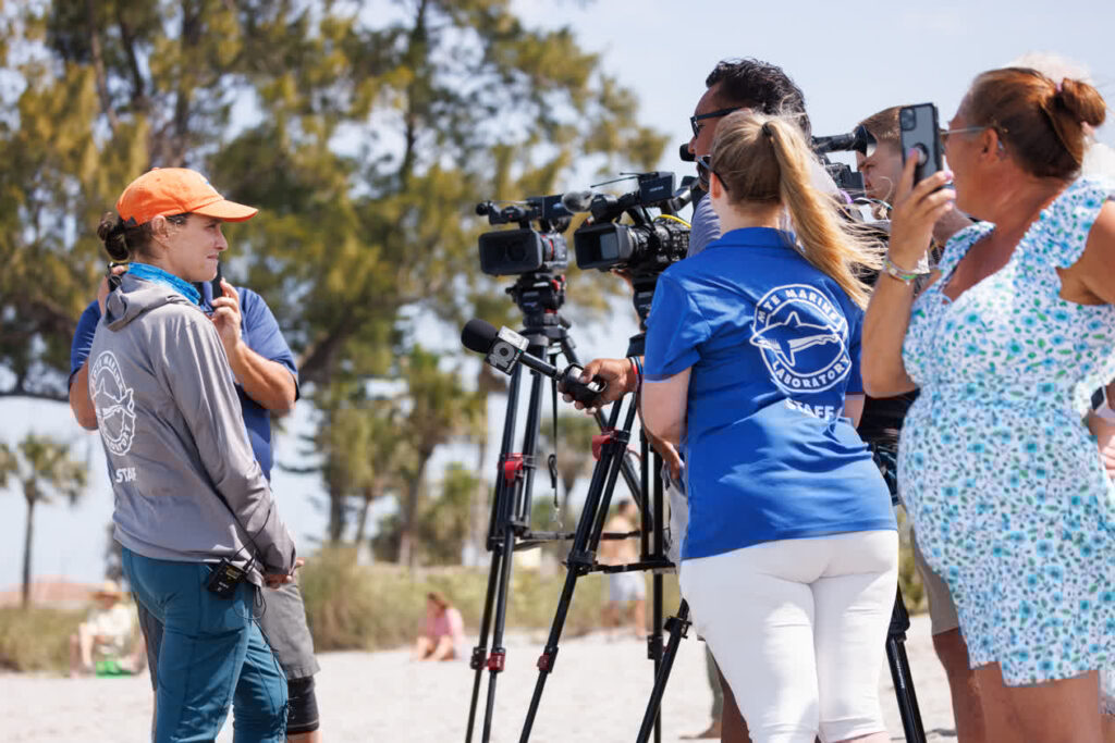 Journalists interview Mote's Gretchen Lovewell on the beach.