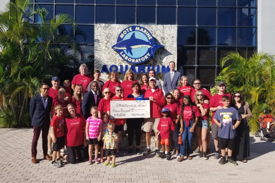 Men, women and children of all ages pose with a giant $15,000 check in front of the Mote aquarium visitor's entrance. Many wear Bank of America shirts.