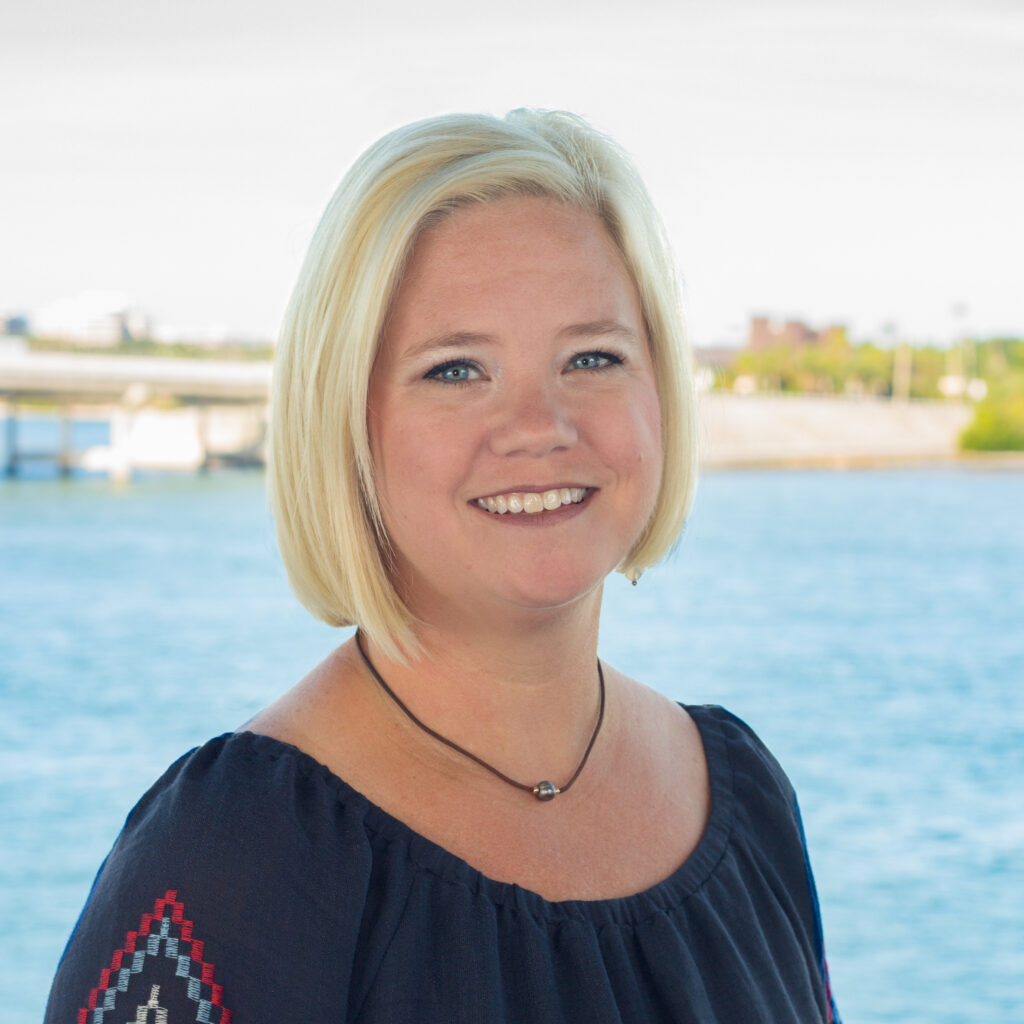 Portrait of Allison Delashmit. She smiles at the camera in font of the bay.