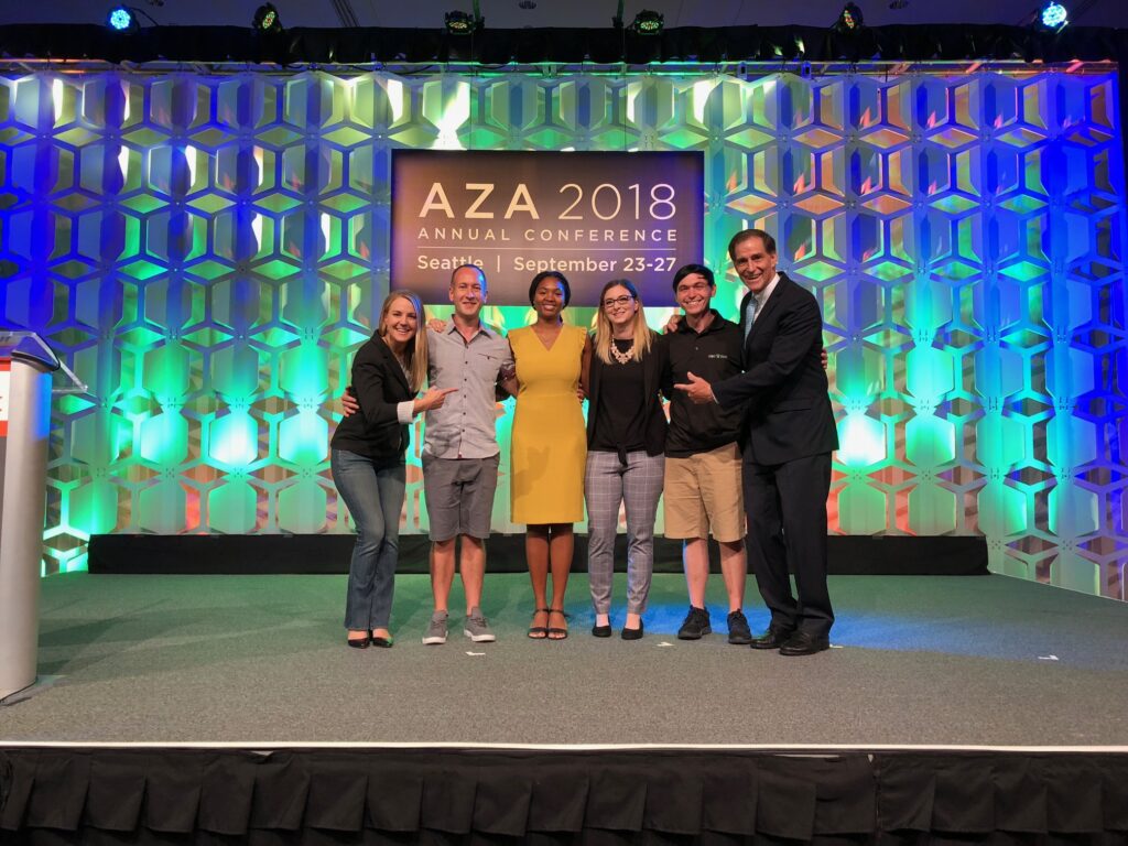 Amanda Hodo stands proud on stage at the AZA 2018 Conference in Seattle with 3 other winners of the 'Find Your Heroes' contest and t2 presenters. She stands in the middle, wearing a yellow dress with her braided hair pulled into a low ponytail.