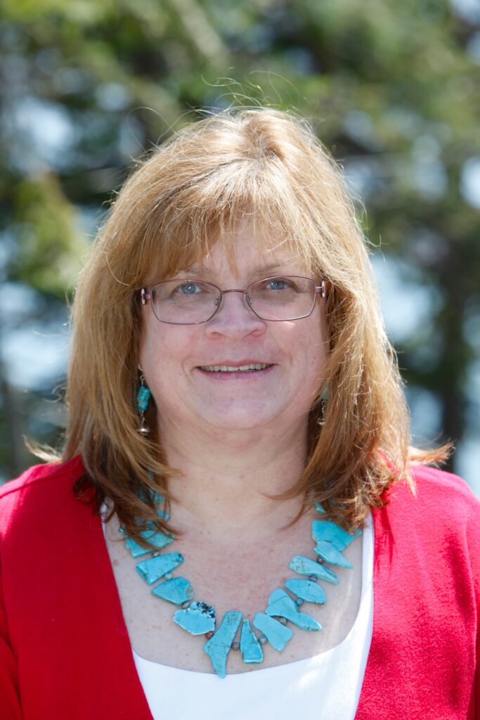 Portrait of Dr. Heil smiling at the camera in front of leafy vegetation.