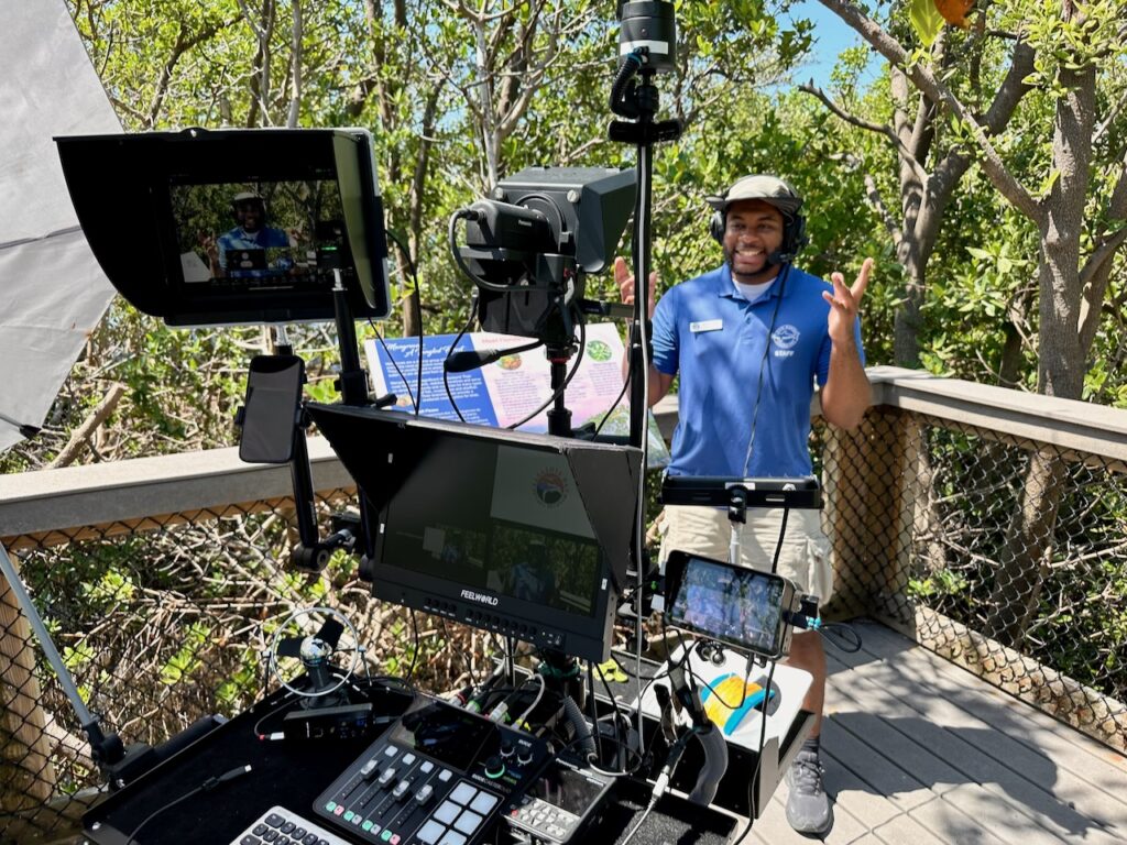 An educator from Mote Marine Laboratory & Aquarium delivers a live virtual program from a mangrove boardwalk using a mobile video cart equipped with cameras, monitors, and broadcast gear.