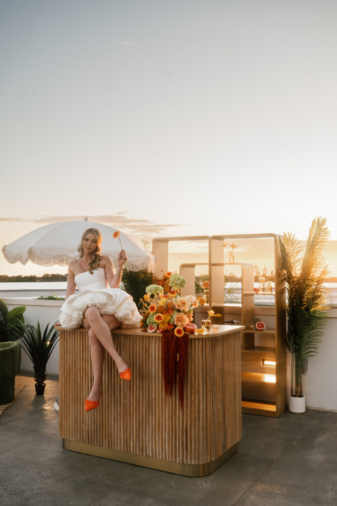 A bride poses holding a flower and sitting on a bar on a terrace